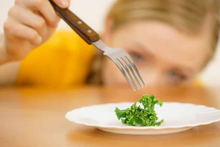 Sad young blonde woman dealing with anorexia nervosa or builimia having small green vegetable on plate. Dieting problems, eating disorder.