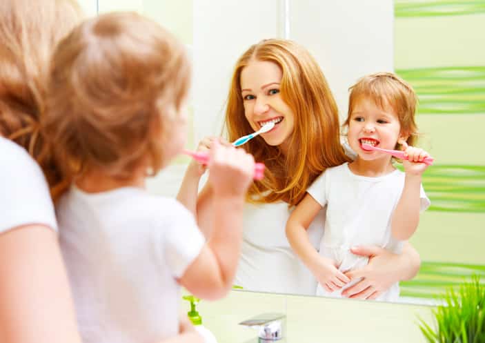 happy family mother and daughter child girl brushing her teeth toothbrushes front of the mirror in the bathroom