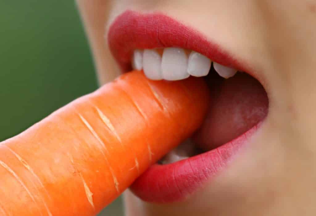 Woman eating carrot with sensitive teeth